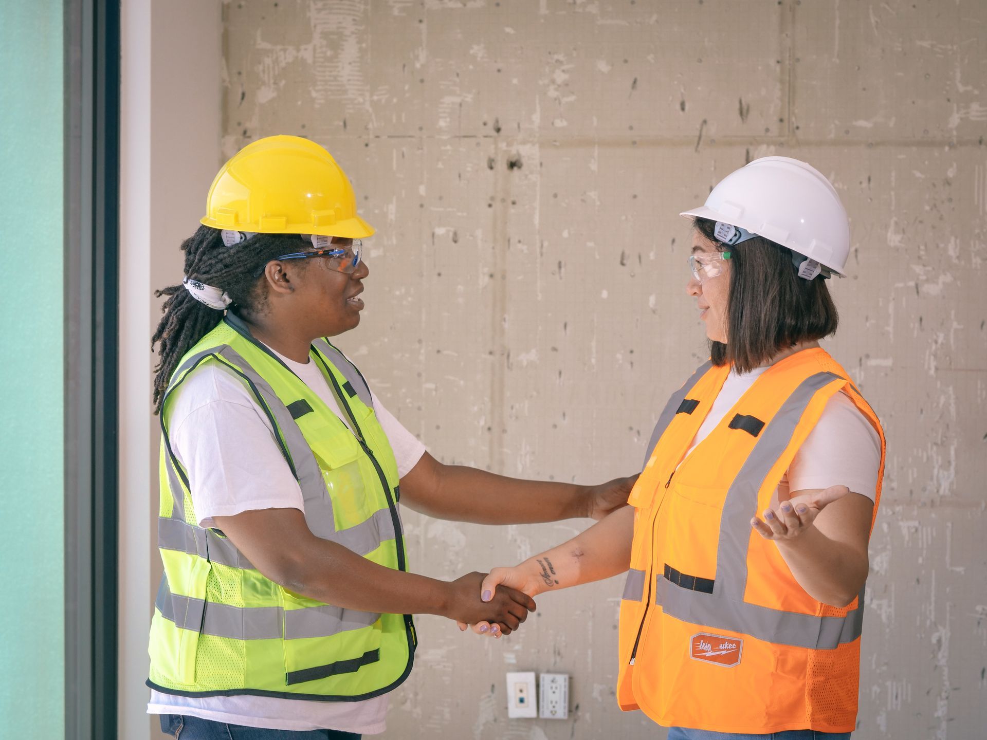 Two Houston tradespeople in hard hats and safety vests shaking hands at a job site